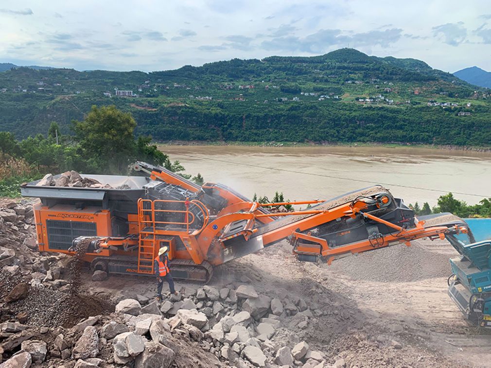 Rockster R1100DS in China: Aufgabematerial Granit mit bis zu 1000mm Durchmesser. Feines, erdiges Material wird durch die Vorabsiebung und das Seitenaustrageband entfernt, noch bevor es in die Brechkammer gelangt.